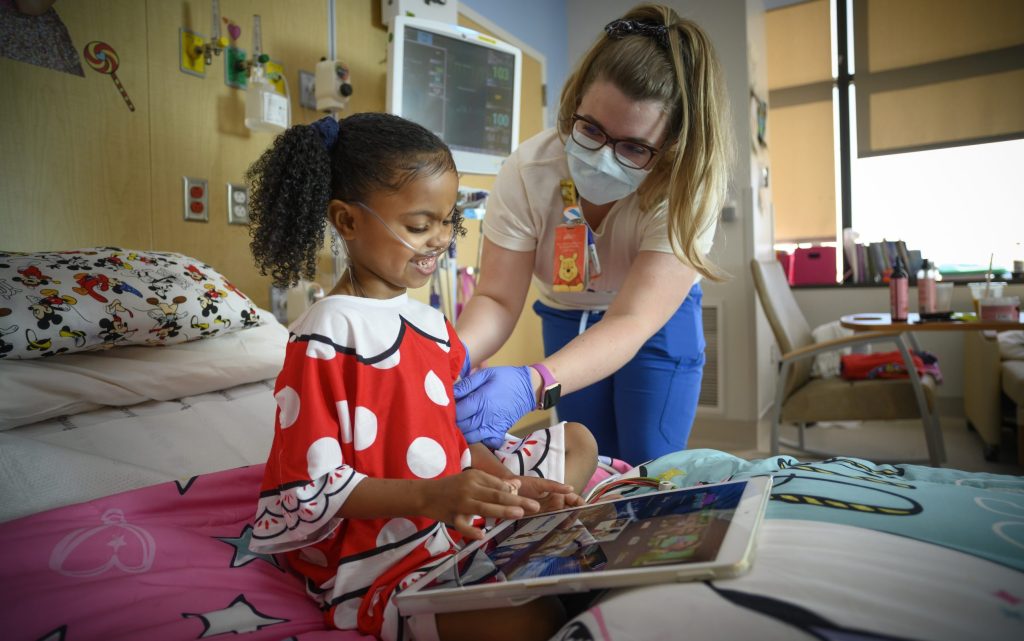 Child in hospital looking at iPad with Disney content, accompanied by a nurse