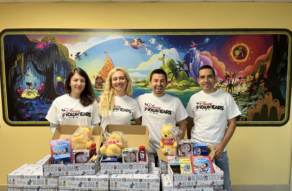 Group of Disney VoluntEARs with stack of packages of Disney plushes, books and toys at an event in Bulgaria